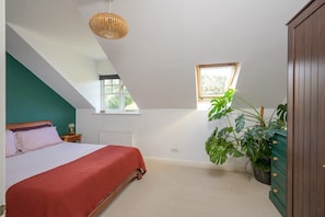 A bedroom with a sloped ceiling, a bed with a red bedspread, a large window, and a potted plant. - Townhouse on the River, Decking & Private Parking (Bristol City)