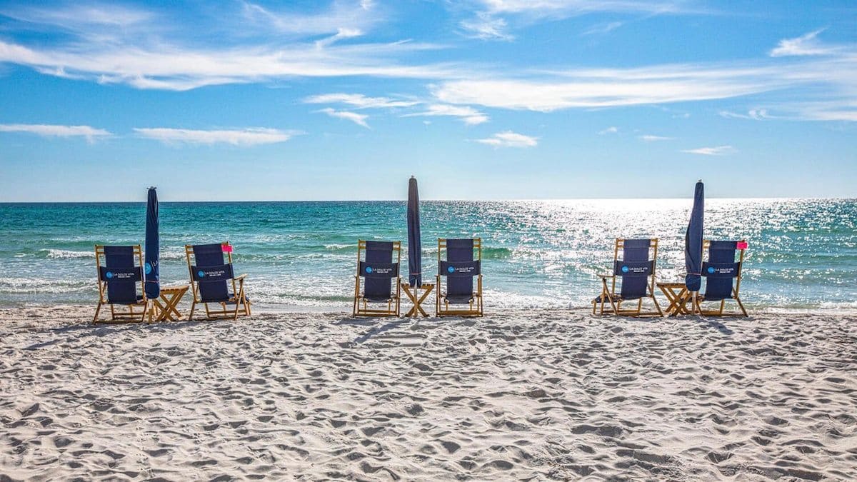 Une plage avec quatre chaises longues et des parasols alignés en rangée, face à l’océan.