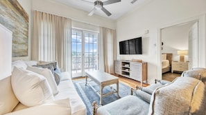 A spacious living room with a sofa, armchair, coffee table, and a television mounted on the wall. - Village of South Walton F307-Vitamin Sea | Condo | Pool & Hot Tub | Sleeps 8 (Alys Beach)