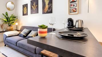 Een moderne woonruimte met een bank, een bijzettafeltje, een eettafel met bestek, een potplant en wanddecoratie.