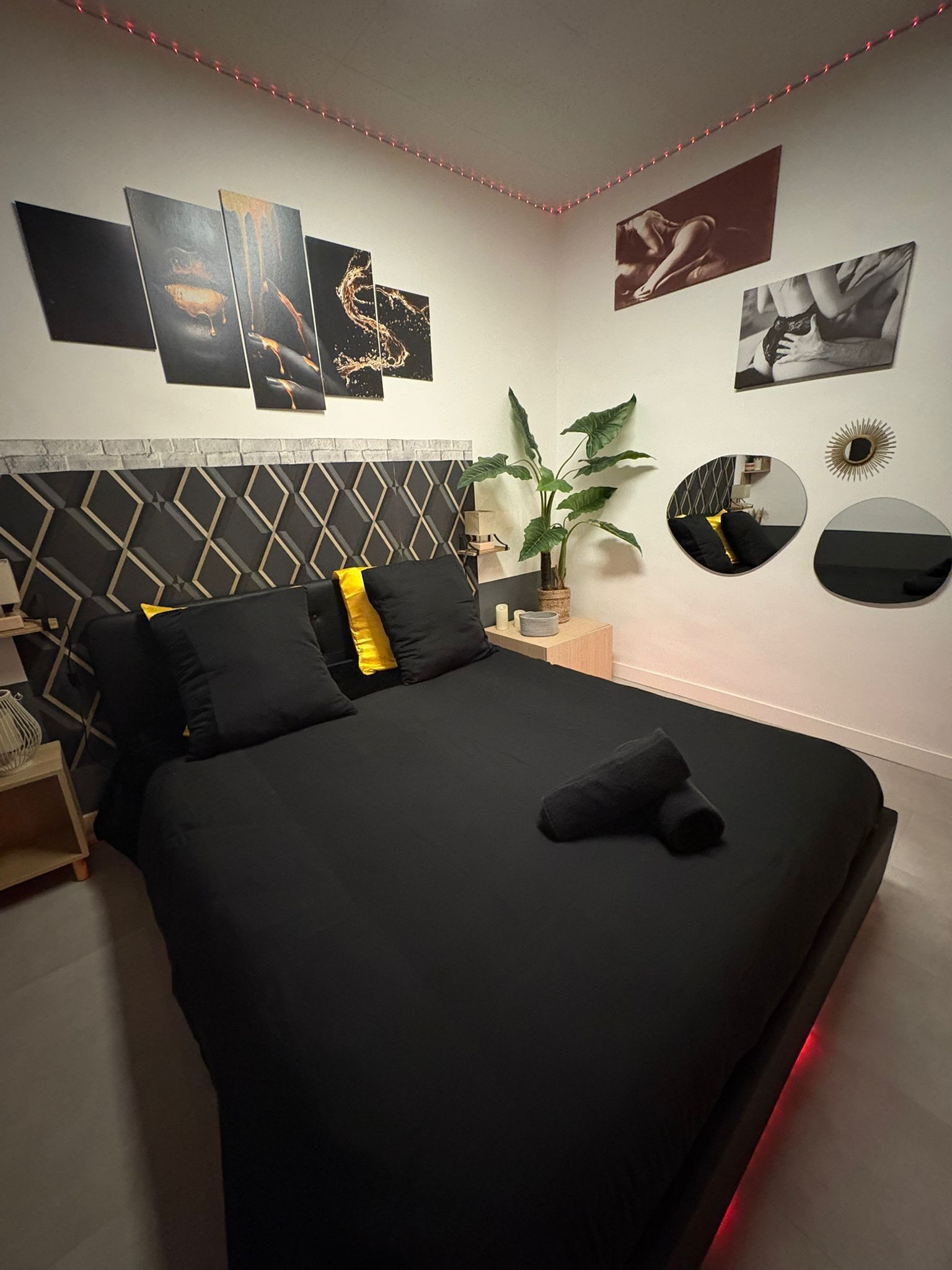 Une chambre à coucher moderne avec une couvre-lit noire, une tête de lit à motifs géométriques et un miroir fixé au mur.