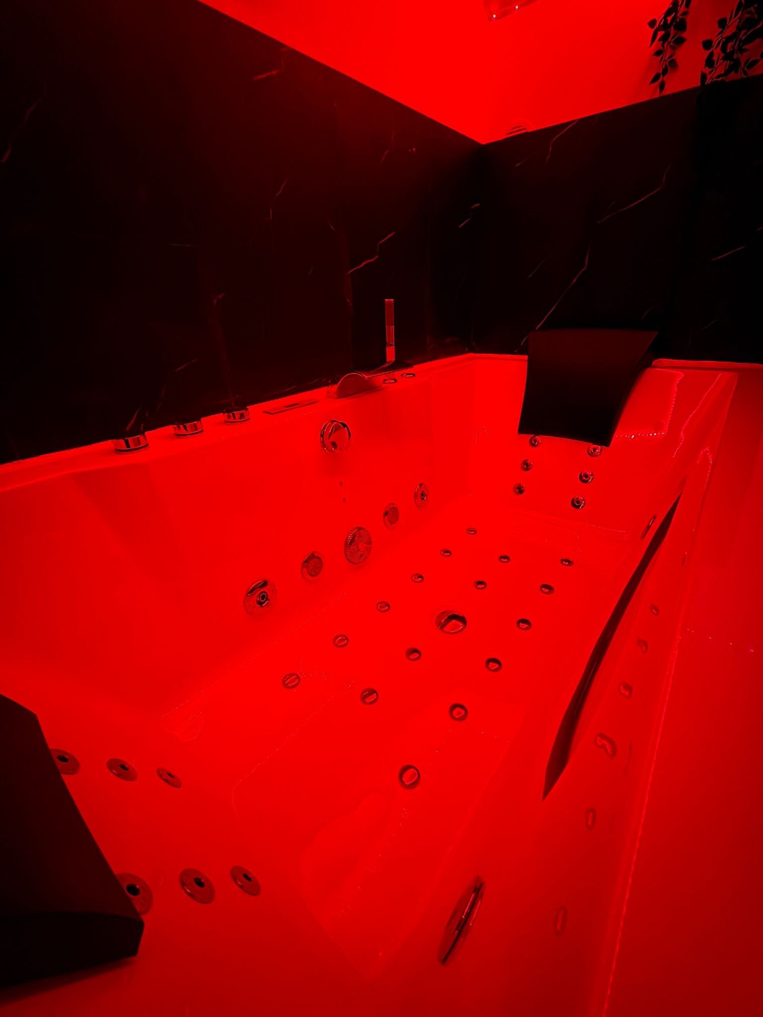 Een kamer in rood licht met een badkuip, een wastafel en een spiegel.