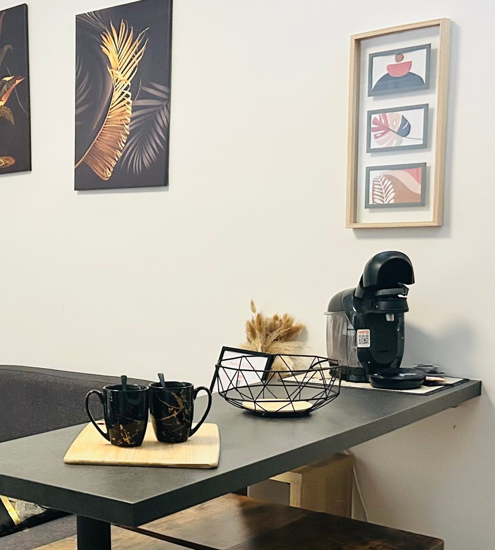Une table avec deux tasses noires, un vase blanc contenant des plantes séchées et une machine à café noire.