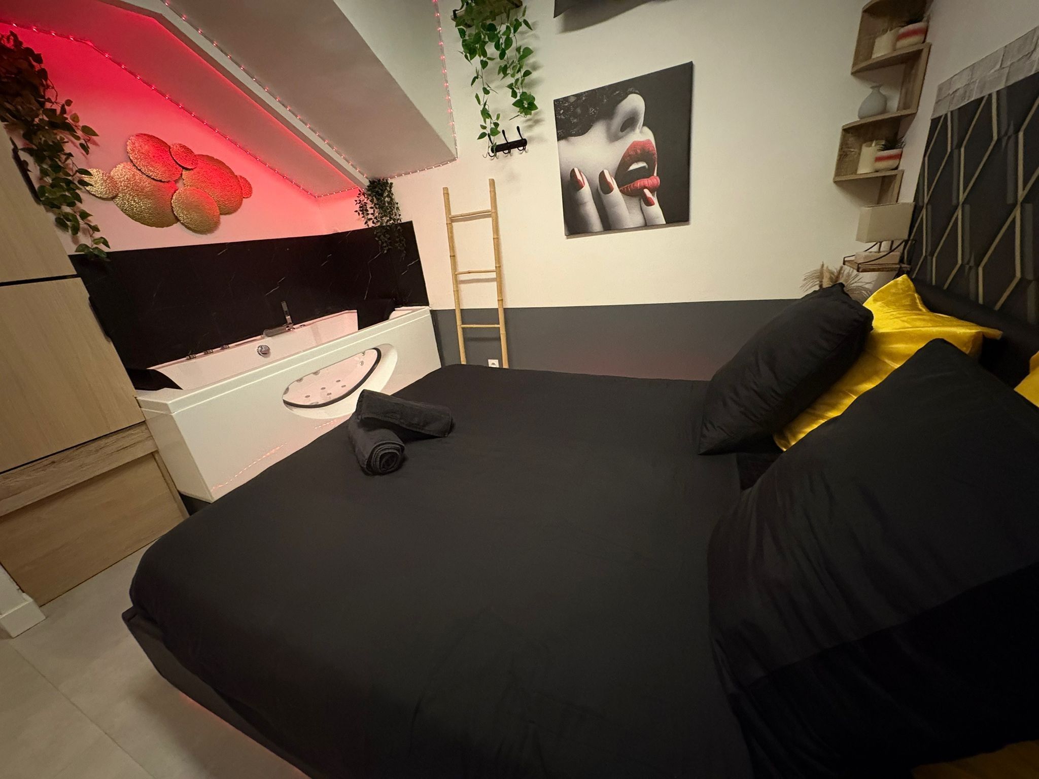 Un dormitorio con cama, un aparador blanco, cabecera negra, un cuadro en la pared y una escalera.