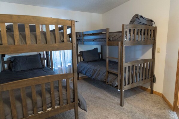 A room with three bunk beds, each with a wooden frame and grey bedding.
