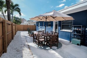A patio with a table and chairs, a wooden fence, and a blue building with windows. - This Must Be The Place (Redington Shores)