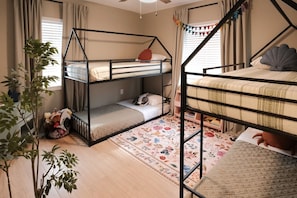 A bunk bed room with a wooden floor, a floral rug, and a plant. - This Must Be The Place (Redington Shores)