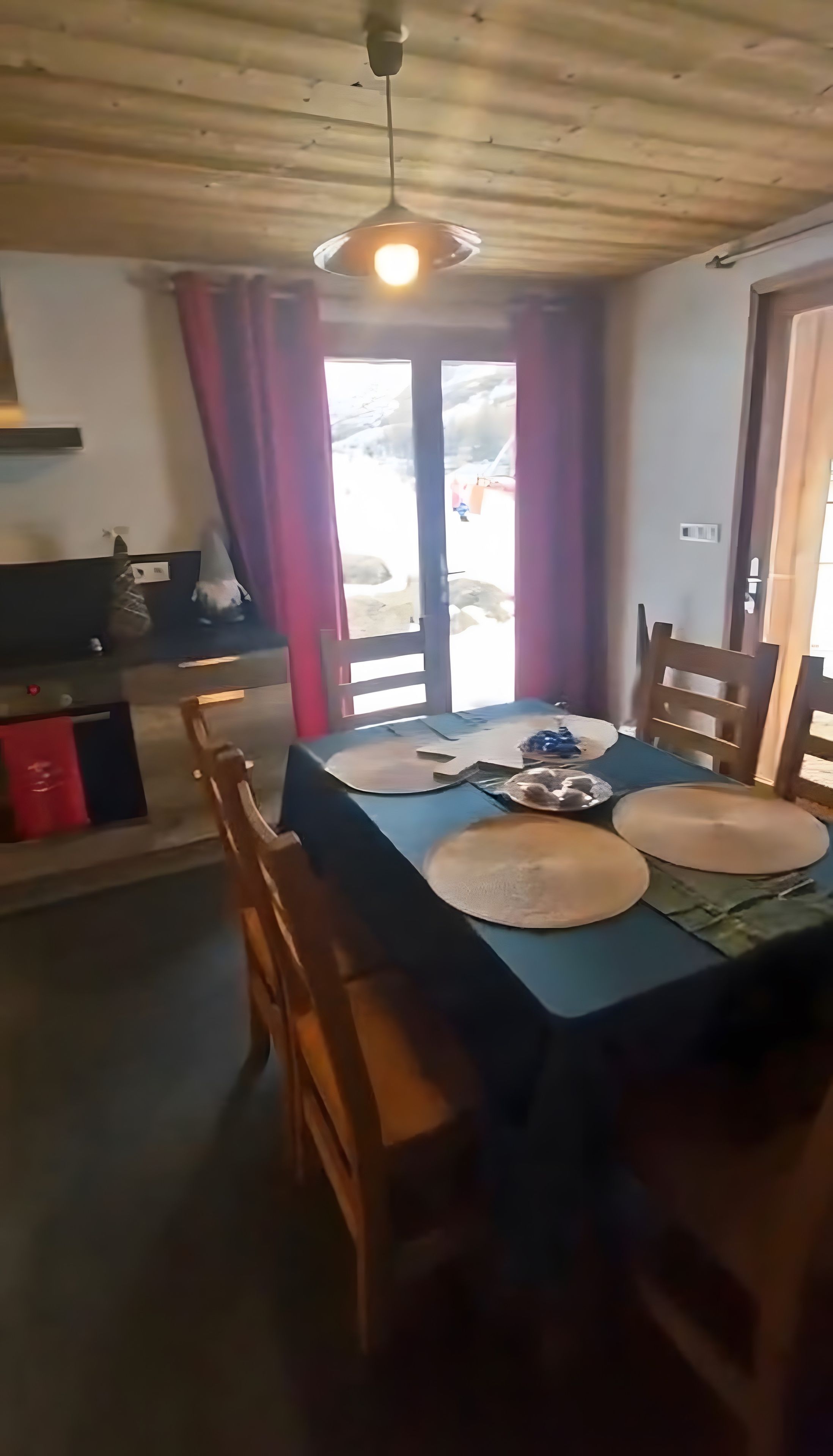 Ein Essbereich mit einem Tisch für zwei Personen, Holzstühlen, einer Deckenleuchte und Blick durch eine Glastür.