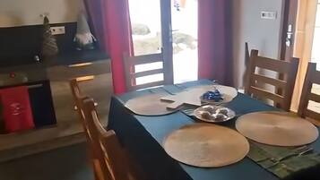 Ein Essbereich mit einem Tisch für zwei Personen, Holzstühlen, einer Deckenleuchte und Blick durch eine Glastür.