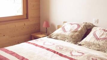 Ein Schlafzimmer mit Holzwand, Fenster, Nachttisch mit Lampe und Bett mit bettenbezogenem Herzmuster.