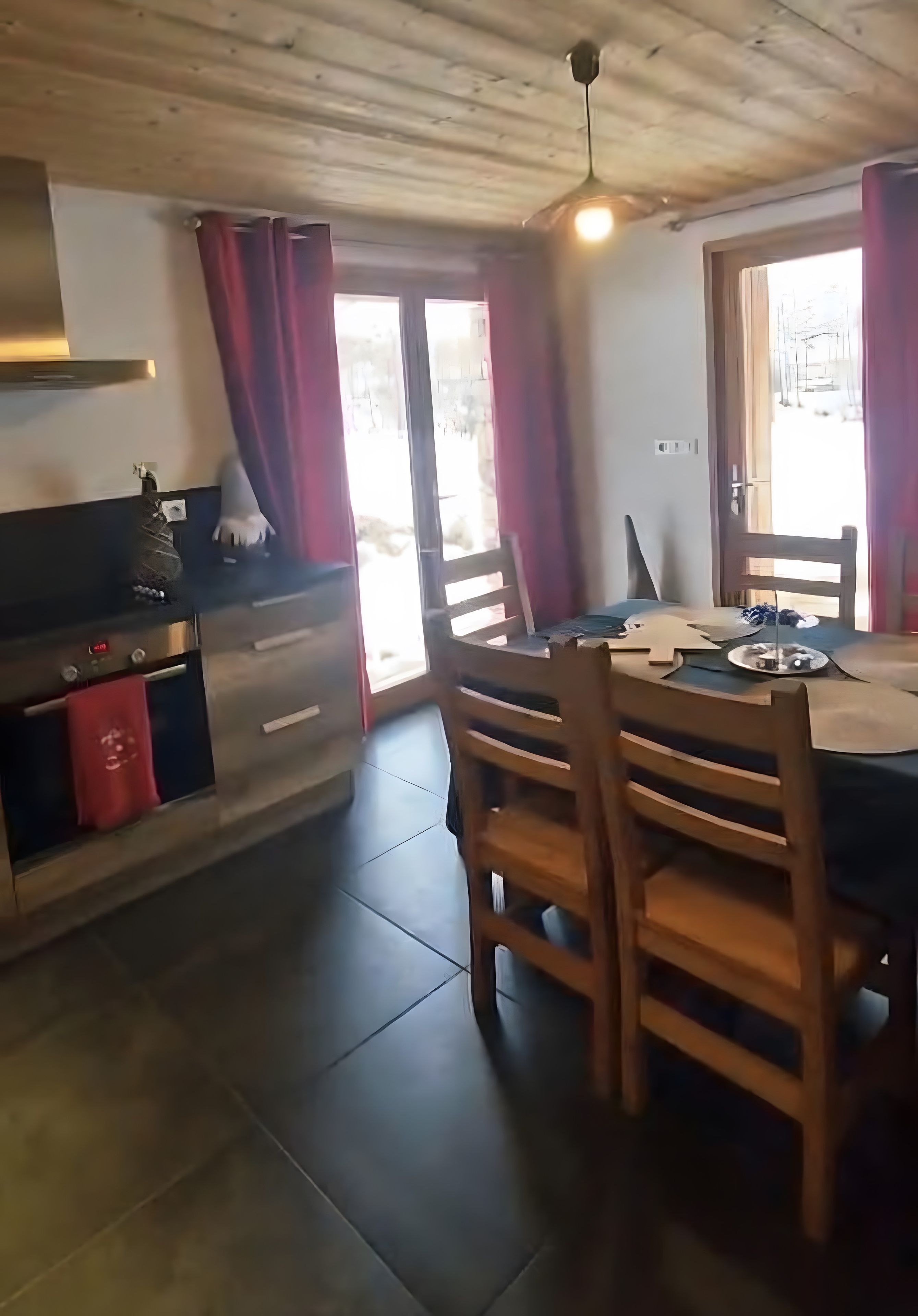 Ein Essbereich mit Holztisch und Stühlen, eine Küche mit Herd und Schränken sowie ein Blick durch eine Glastür.