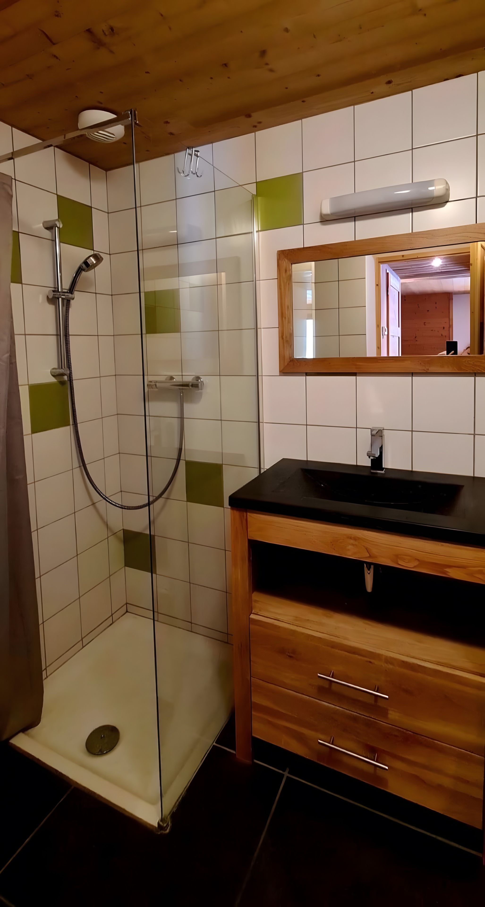 Ein Badezimmer mit einer Duschkabine aus Glas, einem Holzwaschtisch und einem Spiegel darüber.
