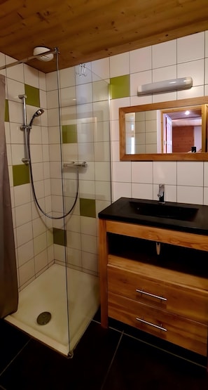Ett badrum med en dusch som är avskärmad med glasväggar, ett handfat i trä och en spegel ovanför handfatet.