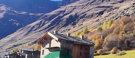 Un paysage de montagne avec une maison en pierre dotée d’un toit en pente et recouverte d’une bâche verte.