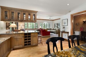 A spacious kitchen with wooden cabinets, a marble countertop, and a dining area with a table and chairs. - Spruce Slopeside Ski-in Access (Avon)