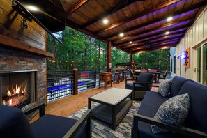 An outdoor patio area with a fireplace, seating, and a view of the forest. - Amenity-Packed! Pool, Pickleball, Sauna, Hot Tub (Broken Bow)