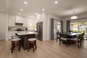 A modern kitchen with white cabinets, a stainless steel refrigerator, and a central island with stools. - Irish Trail Retreat | 1 Mile from ND (South Bend)