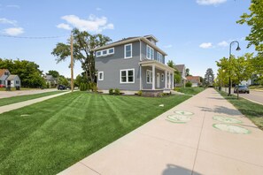 A two-story residential house with a front porch, a well-maintained lawn, and a sidewalk with bike lane markings. - Irish Trail Retreat | 1 Mile from ND (South Bend)