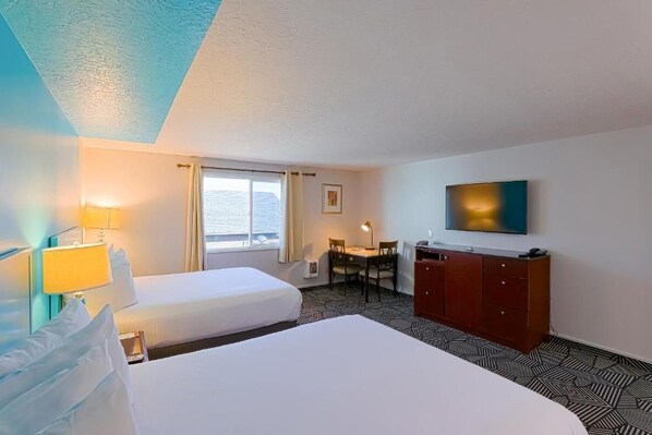 Ein Hotelzimmer mit zwei Betten, einem Schreibtisch, einem Stuhl, einem Fernseher und einem Fenster mit Vorhängen.