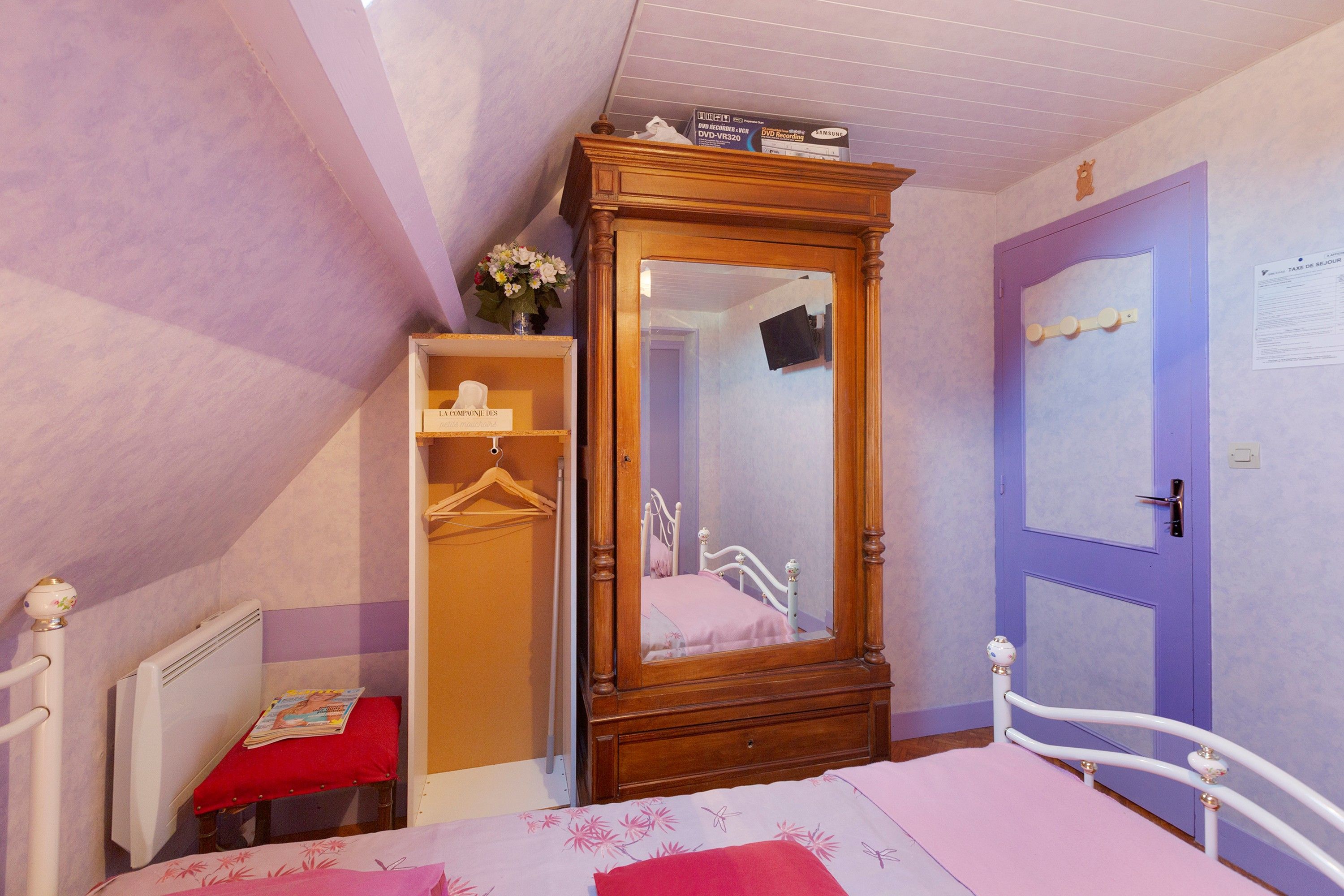 Een slaapkamer met een houten garderobe, een bed met een bloemenprint, een rode stoel en een paarse deur.