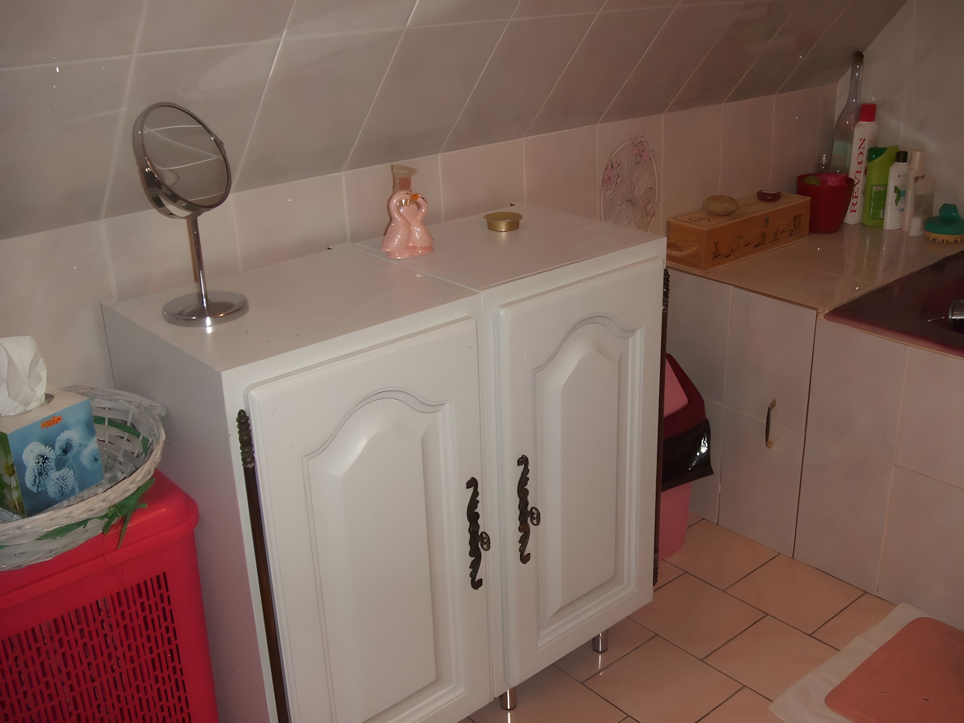 Une salle de bain avec un meuble-lavabo blanc, un miroir, un distributeur de savon rose et des articles de toilette posés sur le comptoir.