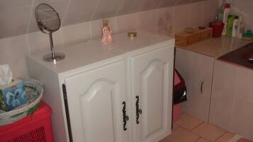 Une salle de bain avec un meuble-lavabo blanc, un miroir, un distributeur de savon rose et des articles de toilette posés sur le comptoir.