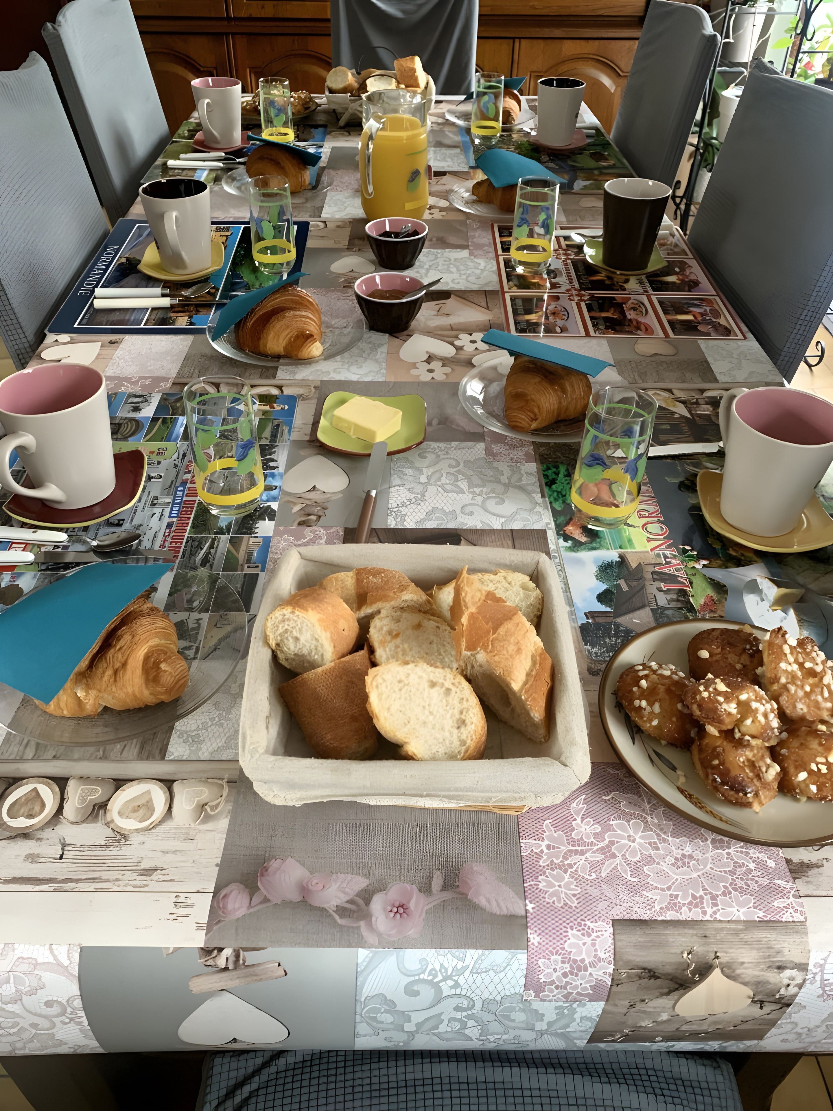 Une table de petit-déjeuner avec des croissants, du pain, du beurre et une carafe de jus d’orange.
