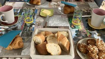 Une table de petit-déjeuner avec des croissants, du pain, du beurre et une carafe de jus d’orange.