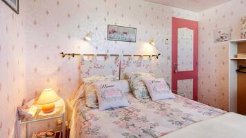 A bedroom with a floral bedspread, two pillows with 'Home' embroidered, a bedside lamp, a framed picture on the wall, and a red door.