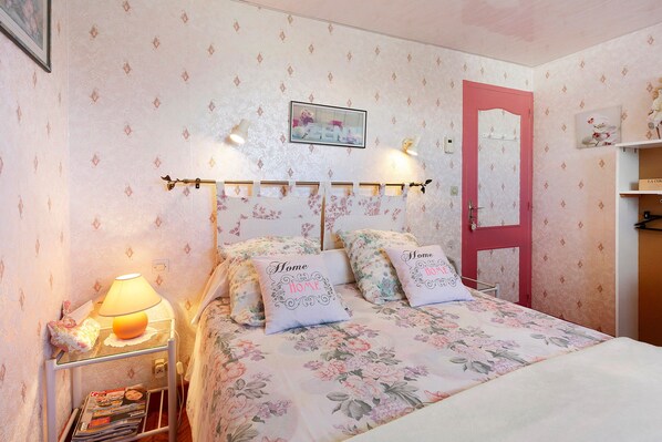 A bedroom with a floral bedspread, two pillows with 'Home' embroidered, a bedside lamp, a framed picture on the wall, and a red door.