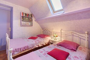 A bedroom with two single beds, a bedside table with a lamp, and a bookshelf against the wall.