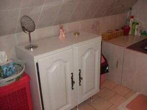 Un baño con tocador blanco, espejo, dispensador de jabón rosa y artículos de aseo sobre la encimera.