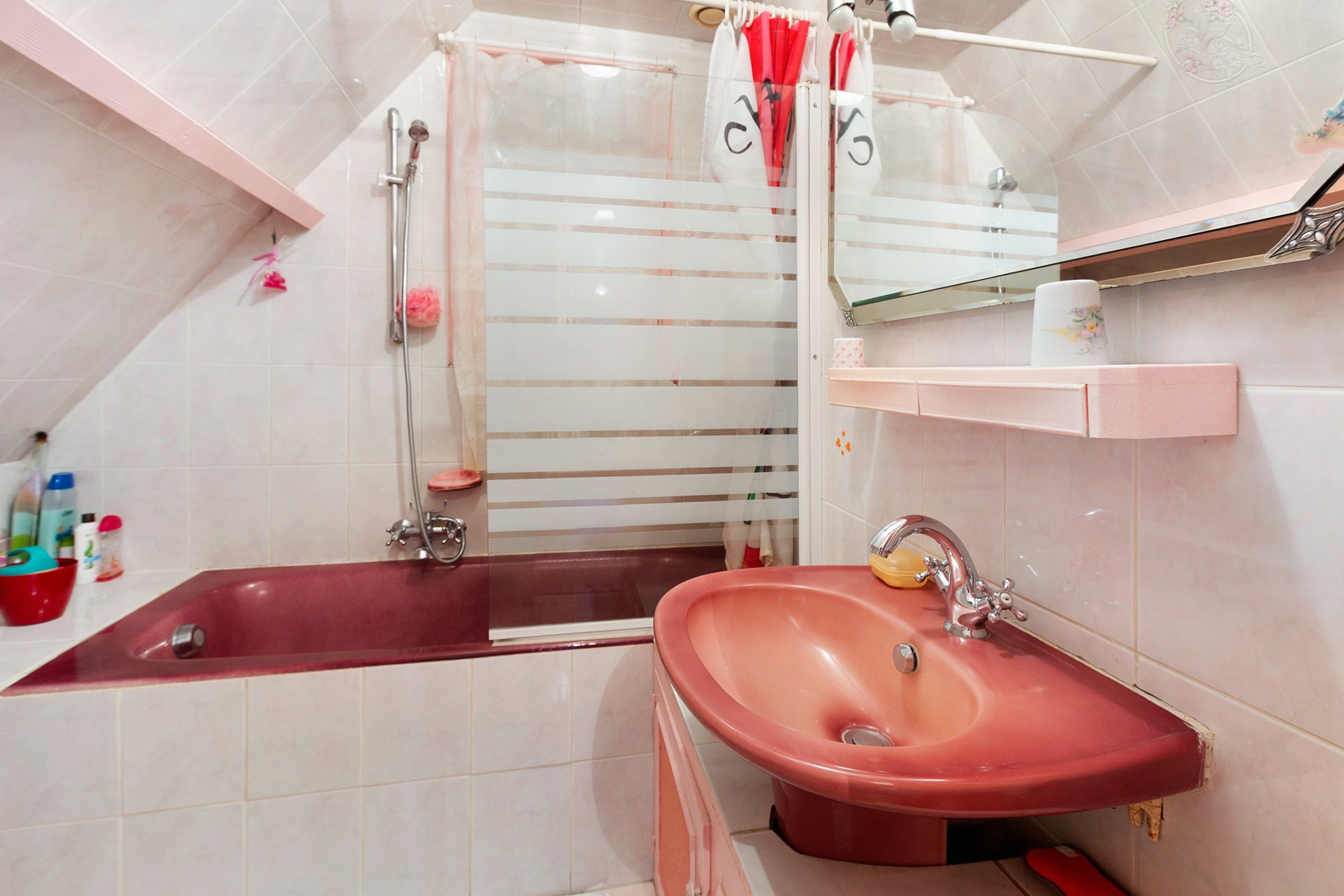 A bathroom with a red bathtub, a pink sink, and a glass shower enclosure.
