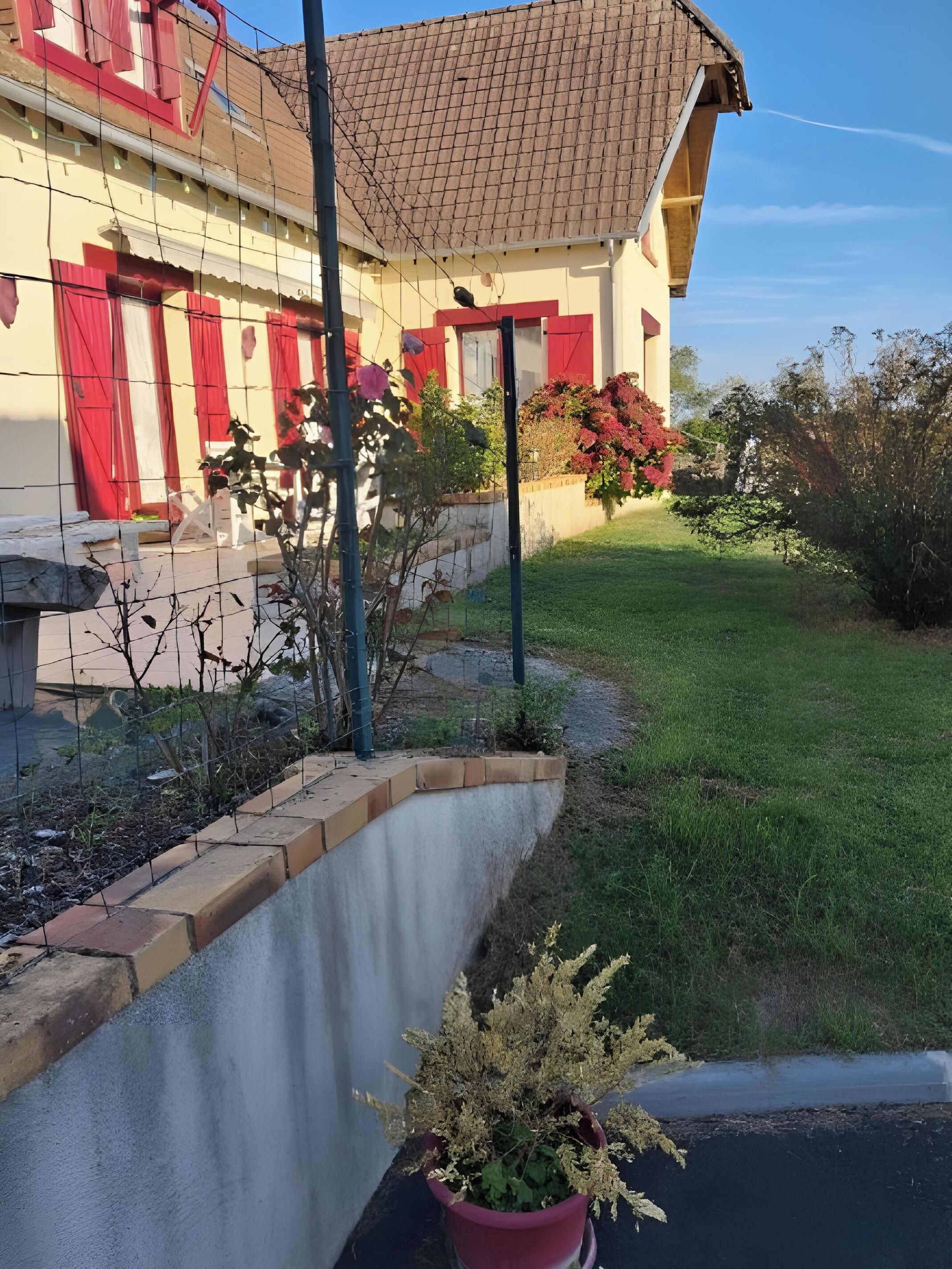 A building with a sloped roof, a fenced garden area with a potted plant, and a clear sky.
