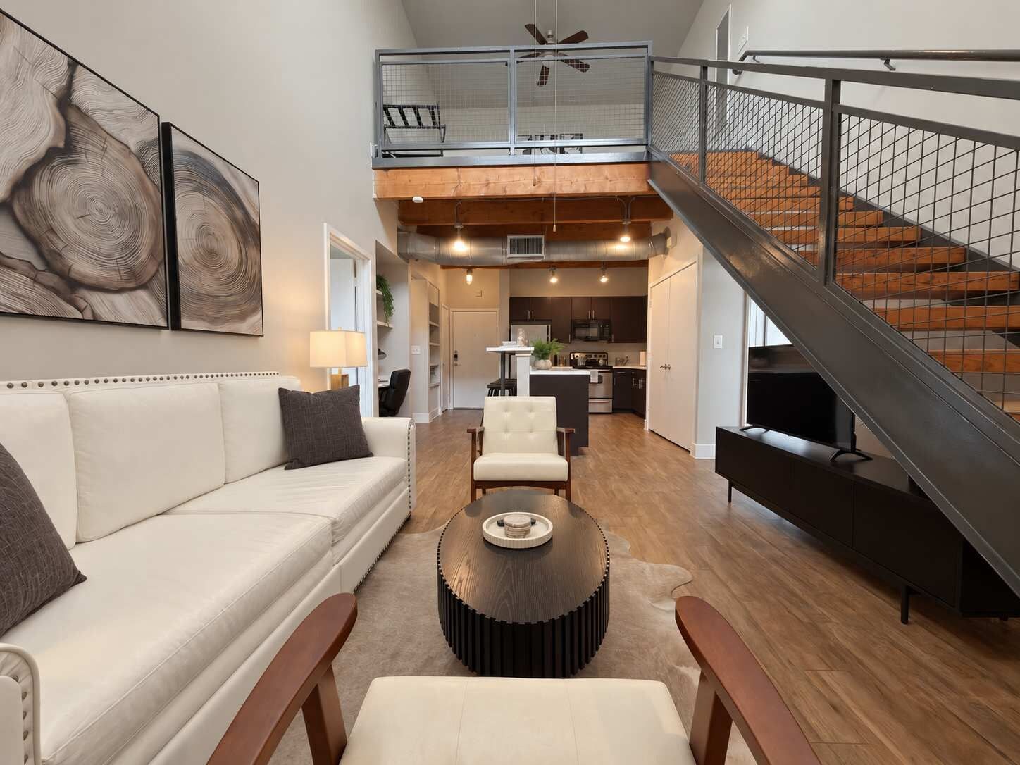 A spacious living area with a high ceiling, a staircase, and a kitchen in the background.