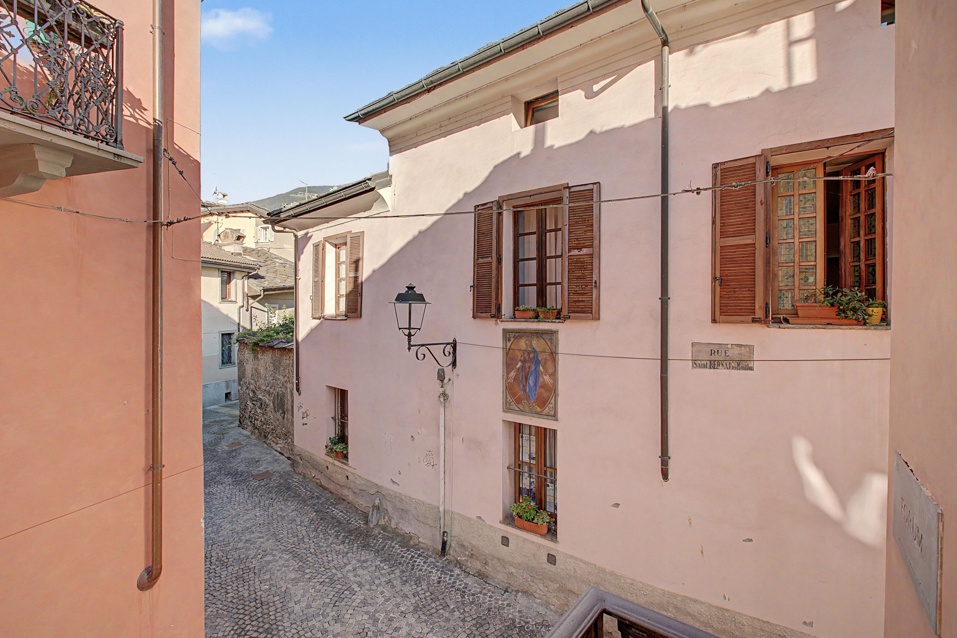 A narrow street with buildings featuring traditional shutters and a street lamp.