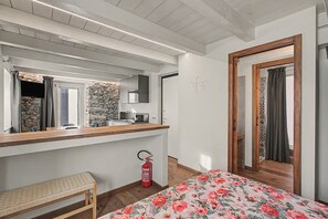 Un dormitorio con una cama de madera, un banco, un extintor y un baño visible a través de una puerta abierta.