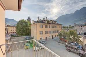 Uitzicht vanaf een balkon op een straat met geparkeerde auto's, een gebouw met een standbeeld bovenop en bergen op de achtergrond.
