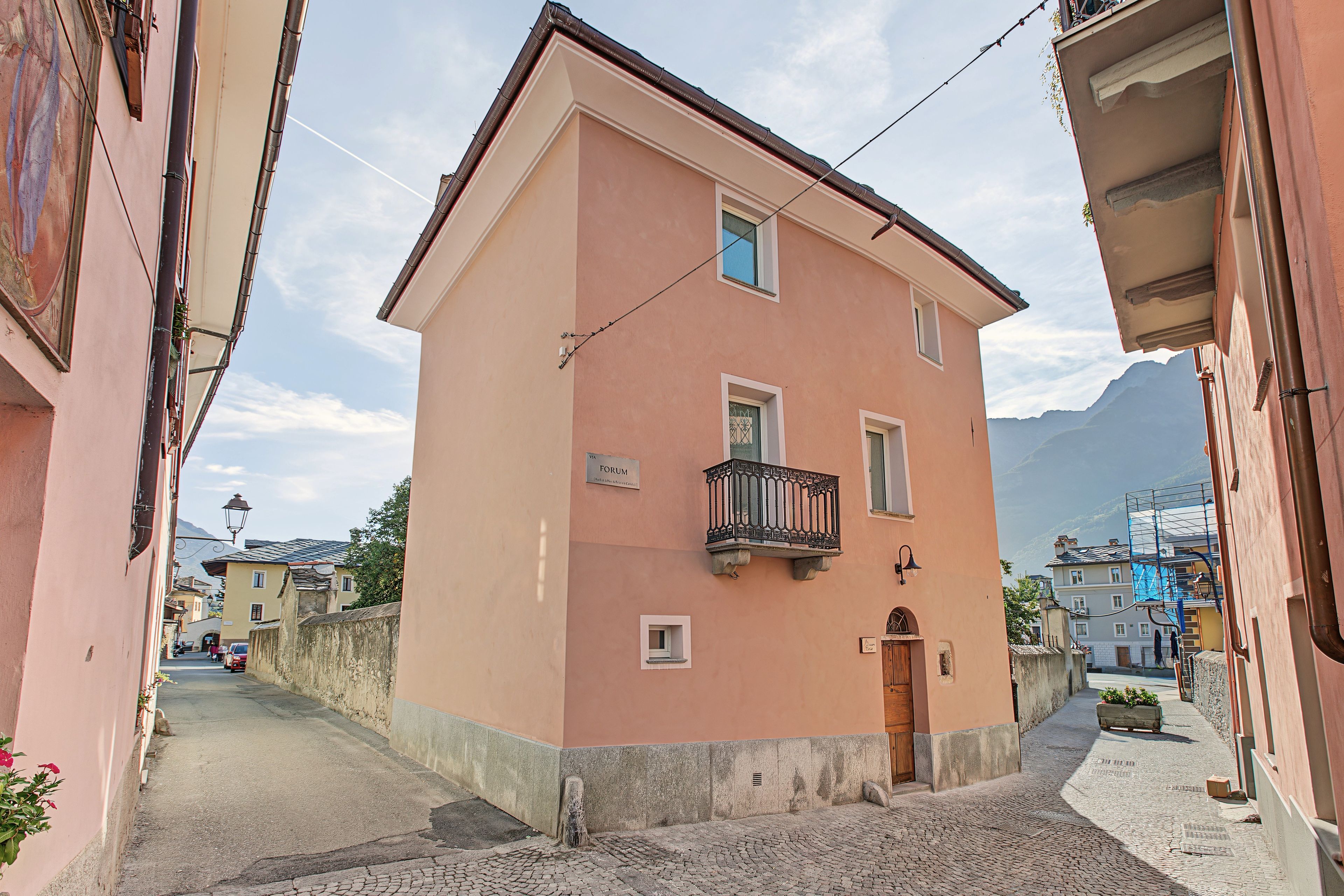 Eine schmale Straße mit einem rosafarbenen Gebäude, das eine Holztür und einen kleinen Balkon hat.