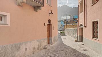 Una stretta strada acciottolata affiancata da edifici con balconi e una montagna sullo sfondo.