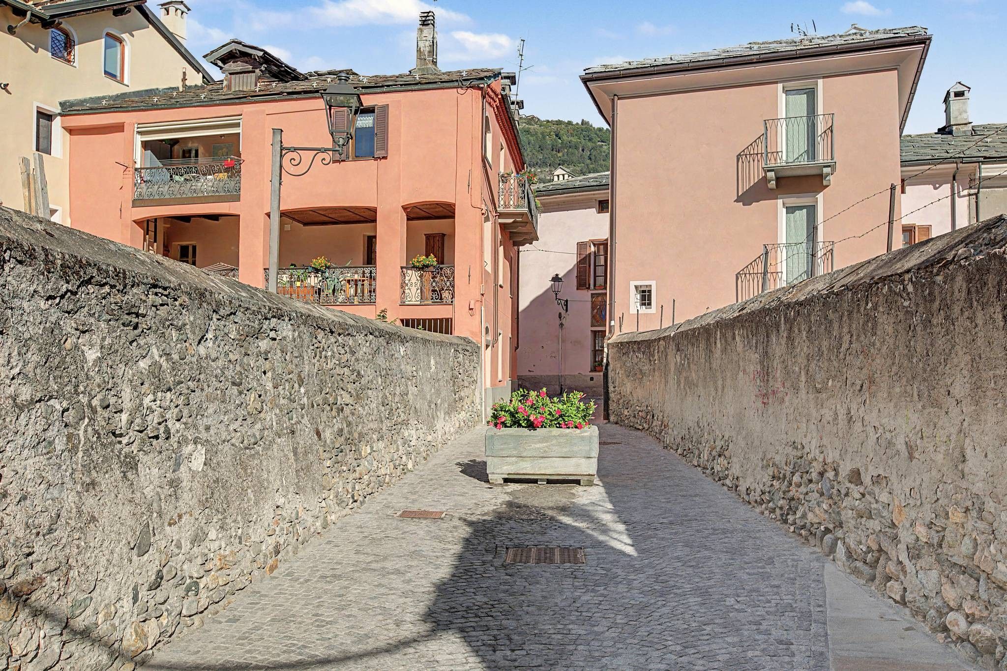 Un estrecho callejón adoquinado flanqueado por muros de piedra y edificios con balcones.