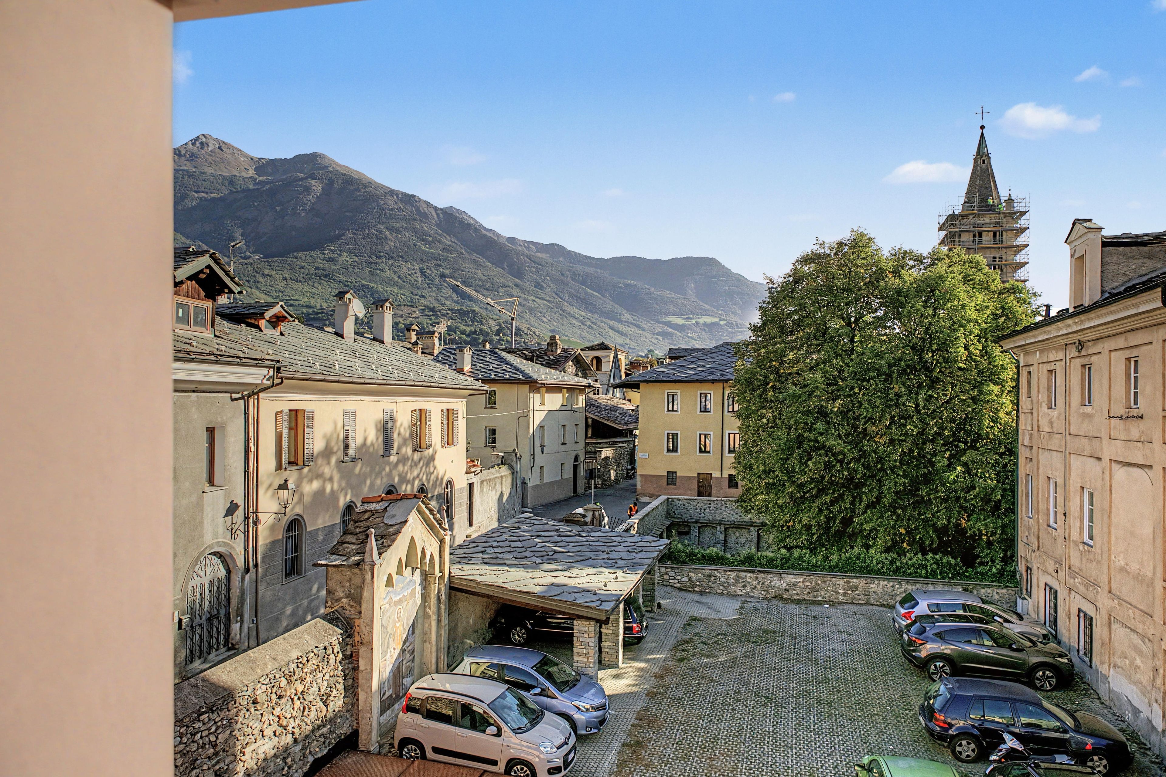 A cobblestone street in a historic town with traditional buildings and a mountain backdrop.