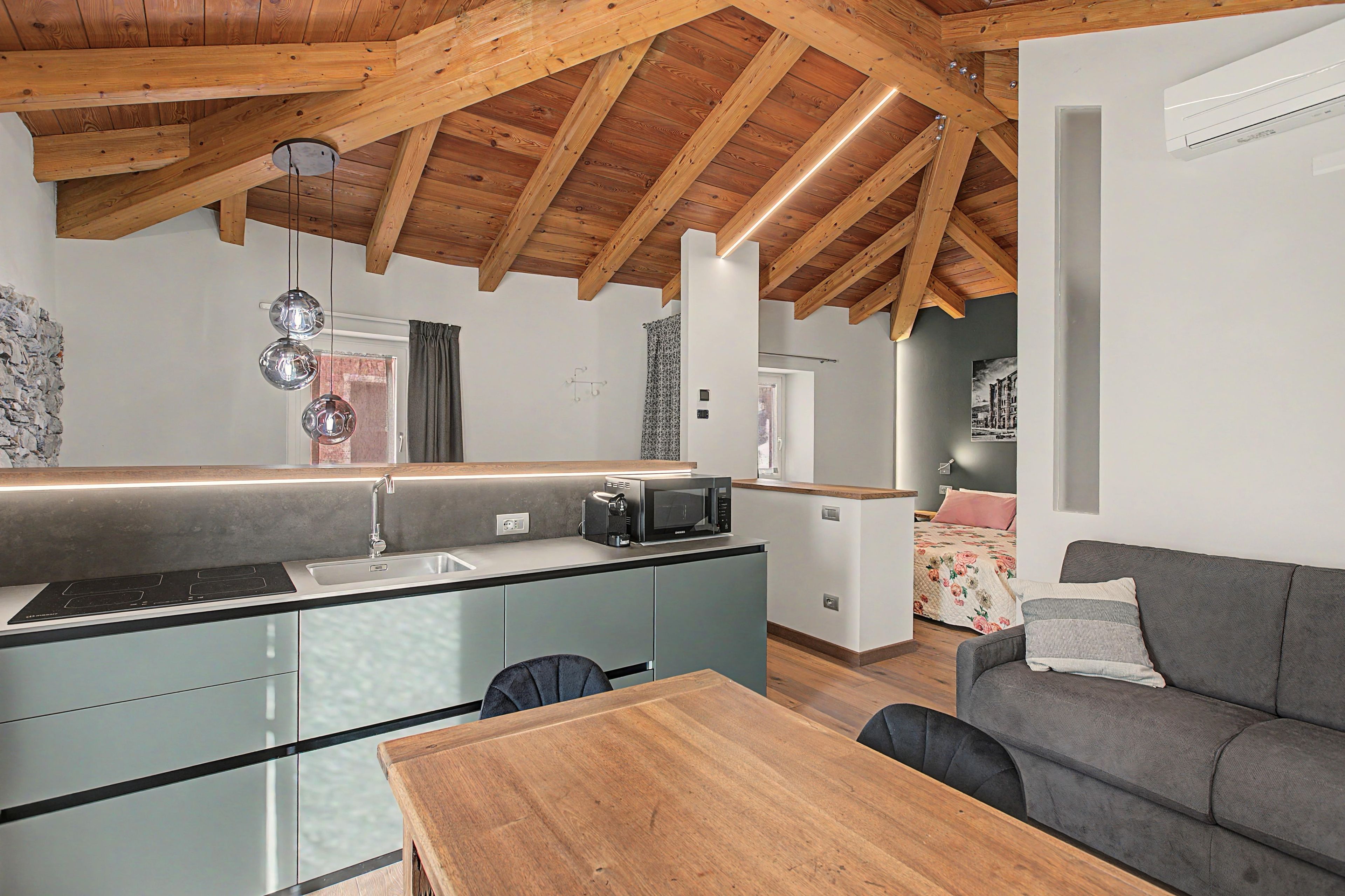 Una cucina moderna con soffitto in legno, isola integrata e un divano grigio nella zona living.