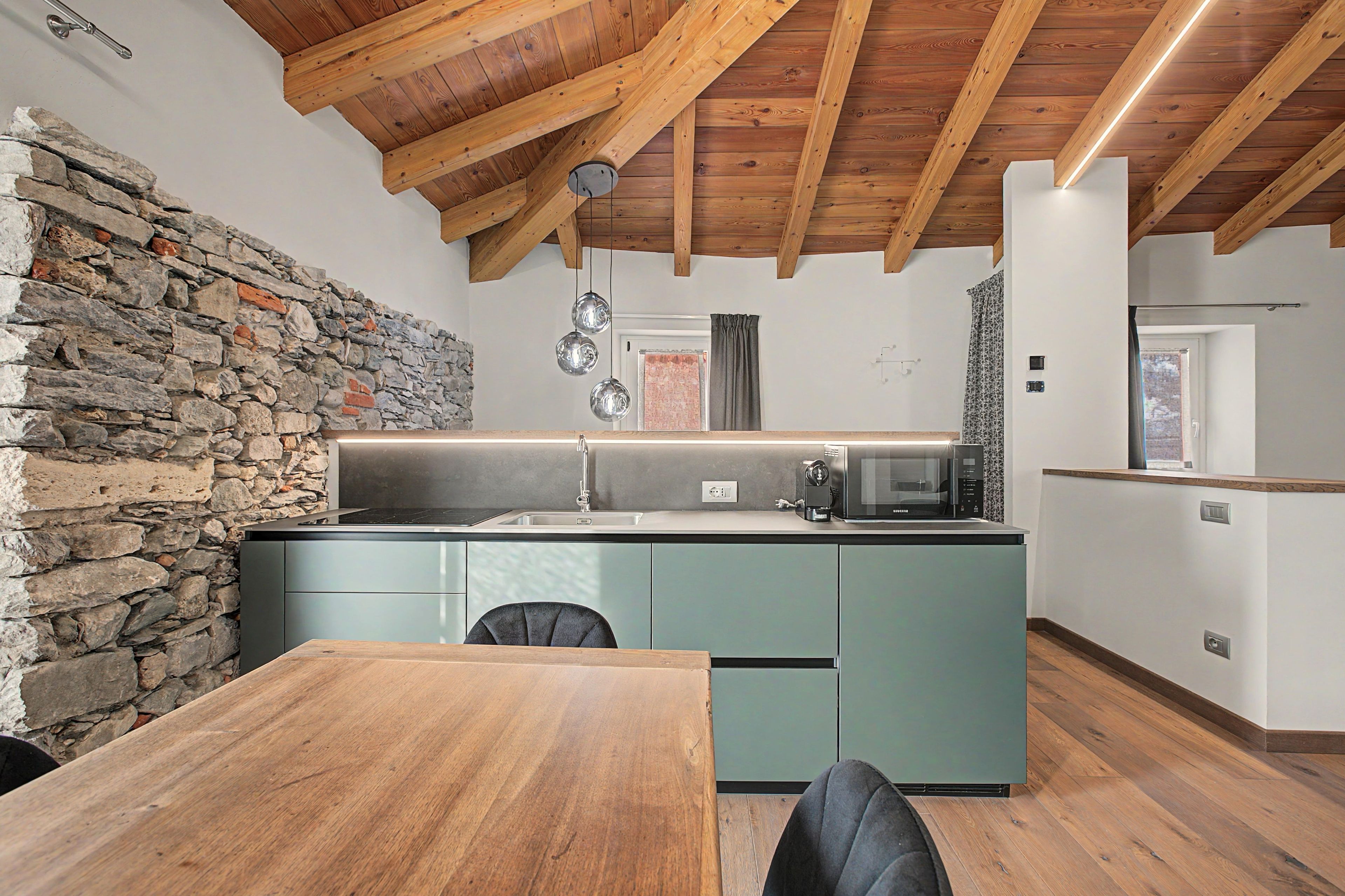 Una cocina con pared de piedra, techo de madera y zona de comedor con mesa y sillas.