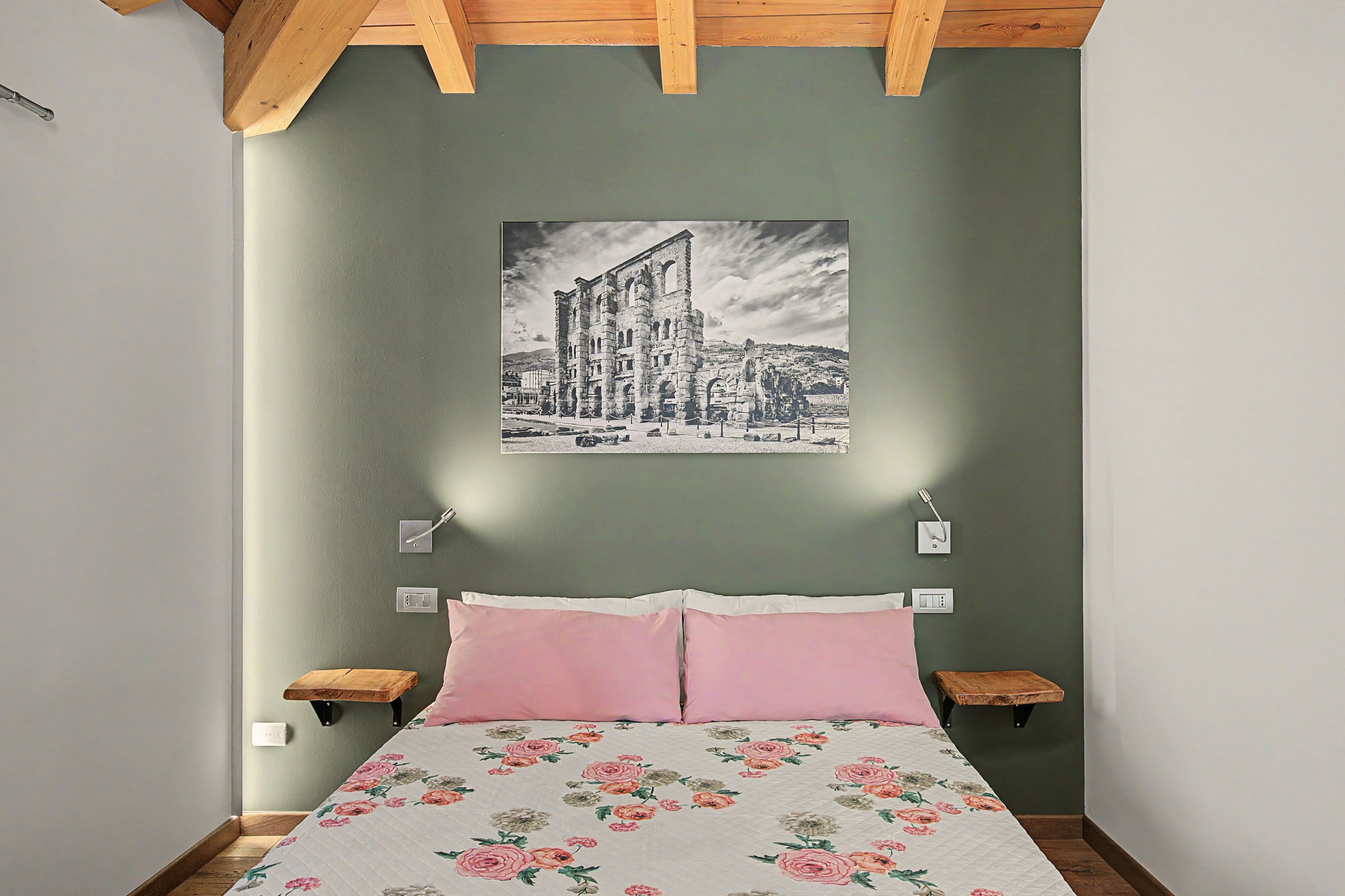Un dormitorio con una cama, dos mesitas de noche, una lámpara de pared e imagen enmarcada.