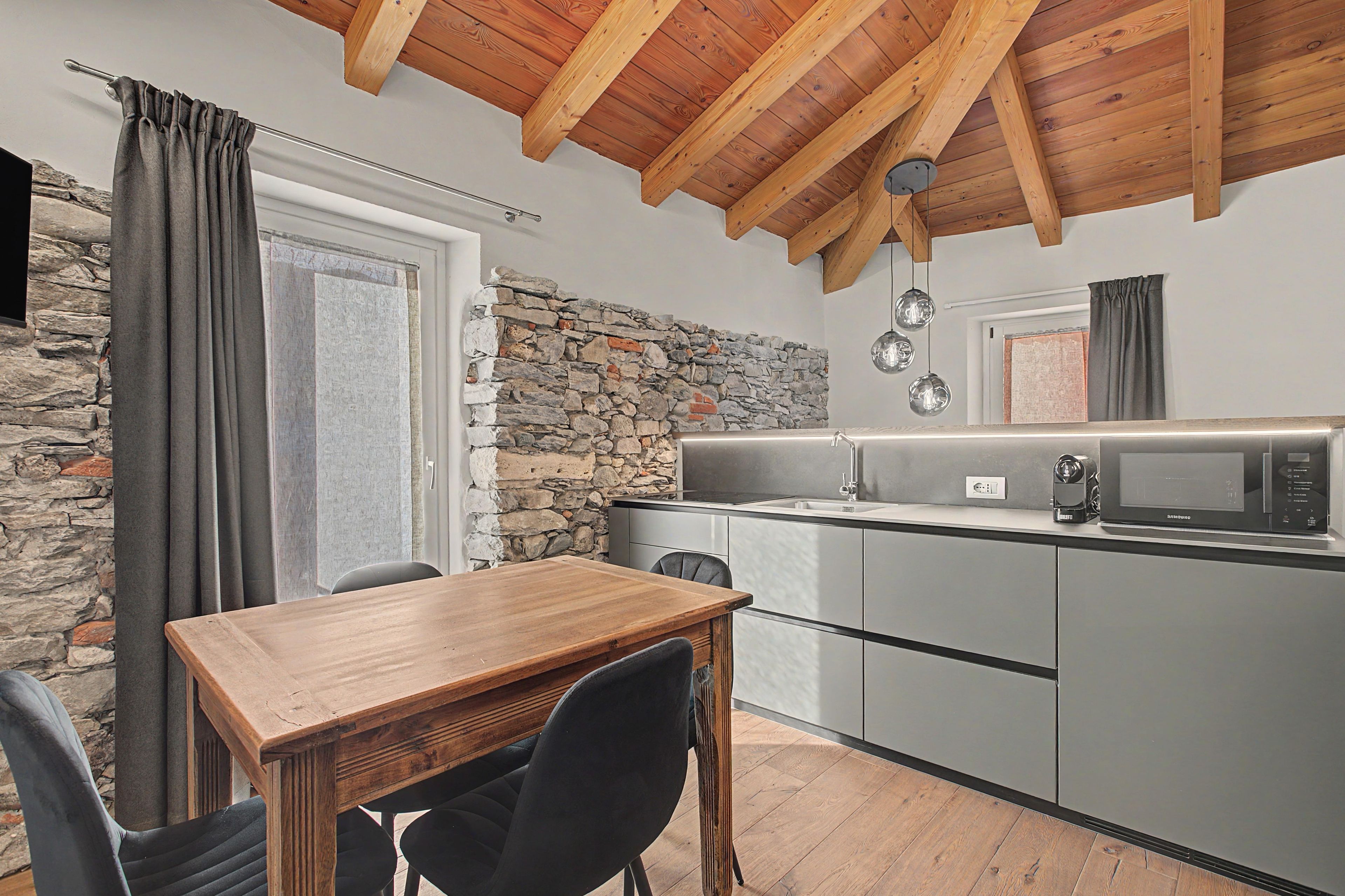Eine kleine Küche mit Steinwand, Holzboden und einem Essbereich mit Tisch und Stühlen.