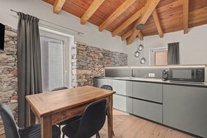 Une cuisine de taille réduite avec un mur en pierre, un plafond en bois et un coin repas comprenant une table et des chaises.
