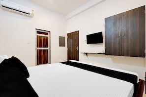 A hotel room with a bed, a wardrobe, a television mounted on the wall, and an air conditioning unit.