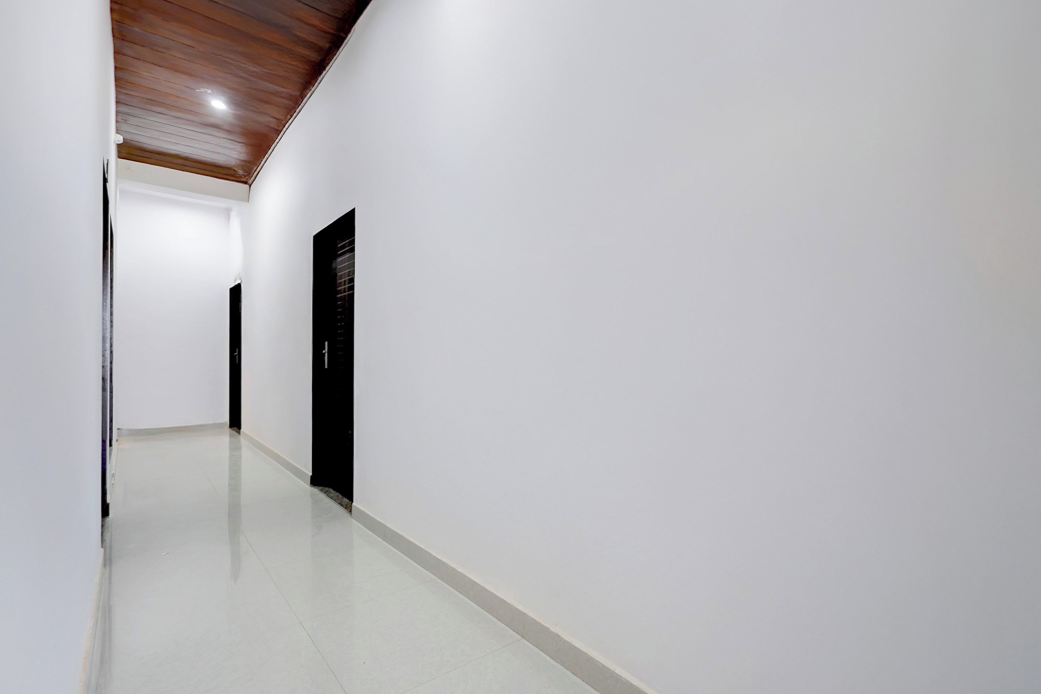 A corridor with a wooden ceiling, white walls, and a black door.