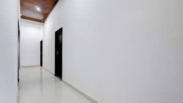 A corridor with a wooden ceiling, white walls, and a black door.